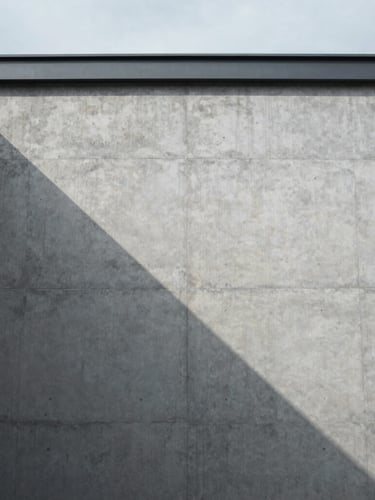Minimalist architectural photography of a concrete facade with sharp geometric shadows, cool overcast daylight, desaturated cool tones, high-contrast composition, 35mm