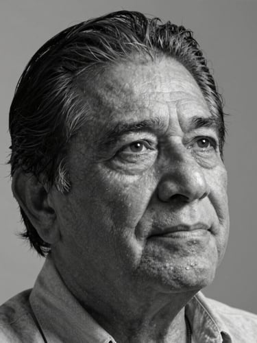 A close-up portrait of a mature Mexican author in black and white, natural side lighting casting deep shadows, serene expression, neutral background