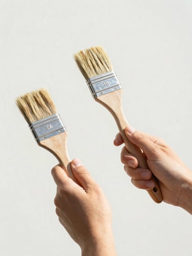 Close-up of hands holding paintbrushes and wooden tools, bright natural outdoor daylight, clean minimalist composition, authentic human action, soft natural tones
