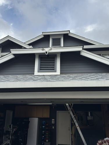 Outdoor home security camera and floodlight mounted on a gray house exterior above a garage.