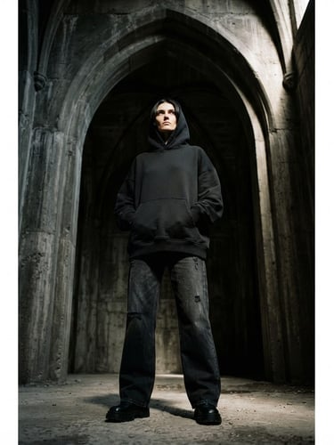 Low-angle heroic shot of a model wearing an oversized heavyweight drop-shoulder black hoodie, standing against a raw concrete gothic arch, harsh chiaroscuro lighting casting deep shadows, 35mm film