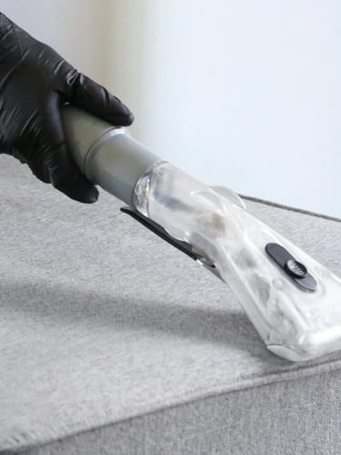 Technician using an extraction tool on a grey upholstered surface.