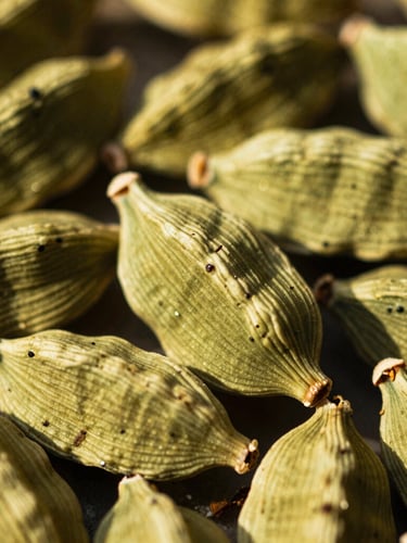 Macro shot of whole green cardamom pods in warm golden-hour sunlight, showing natural textures and fine details, 35mm film