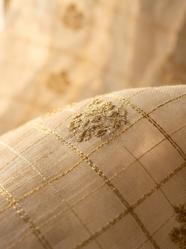 Macro detail shot of translucent ivory Kota Doria fabric with handwoven gold zari threads catching soft golden-hour window light, 35mm
