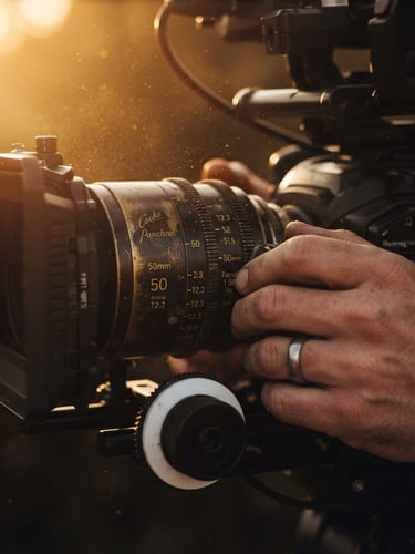 Close-up of hands adjusting the focus ring on a vintage cinema lens, warm golden hour light catching dust in the air, low-key cinematic film photography style