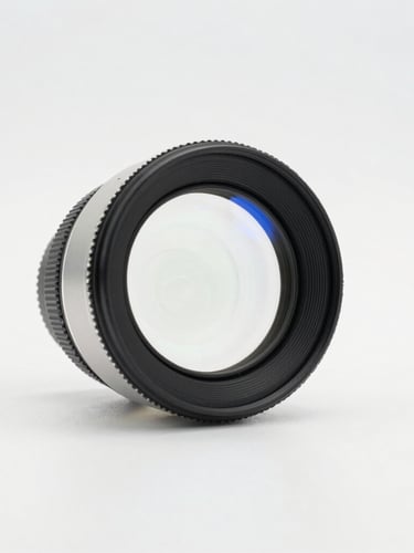 Macro shot of a high-precision optical lens catching bright studio light, clean white backdrop with subtle blue refractions, 50mm lens