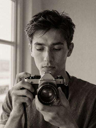 Honest close-up black and white portrait of a photographer holding an old 35mm film camera, soft natural window light, grainy texture, thoughtful expression, neutral background