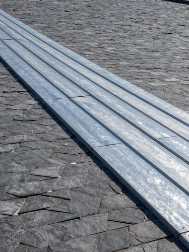 Vue rasante de toitures en ardoise parfaitement alignées sous une lumière matinale, teintes gris ardoise et zinc métallique, mise au point nette, photographie architecturale.