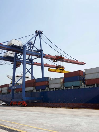 Wide-angle industrial cargo port in bright daylight with heavy container crane loading a shipping vessel, high contrast steel and concrete tones, 35mm