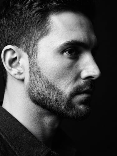 High-contrast black and white photography, close-up of a man's sharp jawline and perfectly groomed beard, dramatic side lighting, deep shadows, premium editorial style, 35mm lens