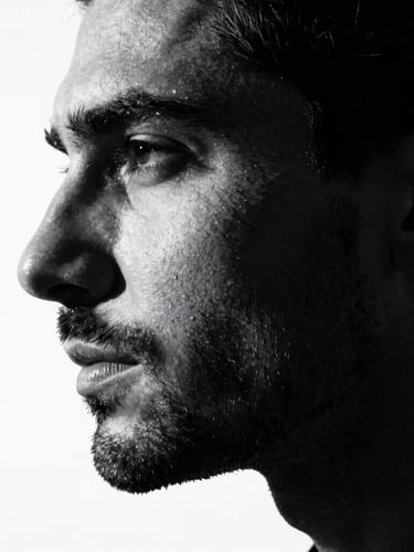 High-contrast black and white portrait of a man of profile with dramatic side lighting, deep shadows, highlighting the clean lines of his beard and skin, premium editorial style.