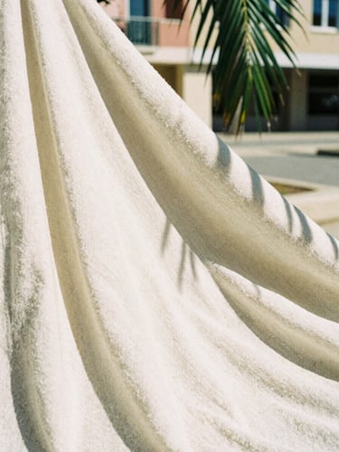 Close-up of thick organic cotton fabric texture, warm direct sunlight casting sharp shadows from a nearby palm leaf, architectural background, 35mm film.