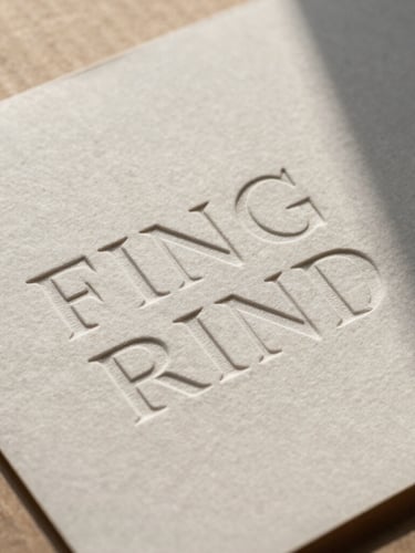 Close-up of embossed typography on heavy textured paper resting on raw cardboard, high-contrast natural light casting sharp shadows.