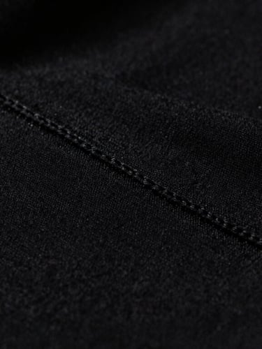 Close-up macro shot of heavy black cotton fabric texture, clean double stitching, dramatic high-contrast side lighting with a faint neon yellow rim light, 35mm.