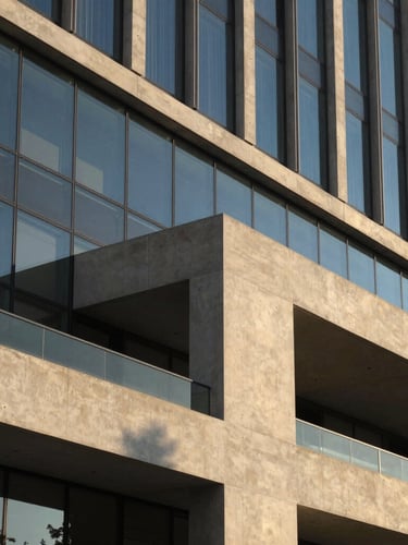 Architectural detail of a modern concrete and glass building facade, clean sharp angles, warm afternoon sunlight casting long shadows, elegant editorial composition