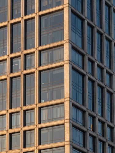 Elegant architectural detail of a modern glass and steel skyscraper facade in Miami, warm golden hour light reflecting off the windows, clean editorial composition