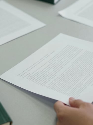 Close-up of hands organizing printed document drafts on a clean slate-gray desk, soft overcast daylight, sharp focus, 35mm