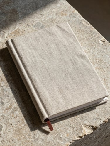 Meticulously styled flat-lay of a custom-designed linen book cover resting on a raw stone slab, soft natural daylight, long shadows
