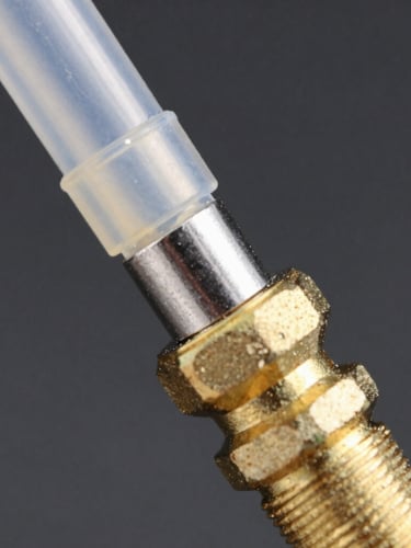 Macro shot of a pneumatic plastic tube securely connected to a brass fitting thread, metallic steel and brass textures, high-contrast industrial lighting, dark background