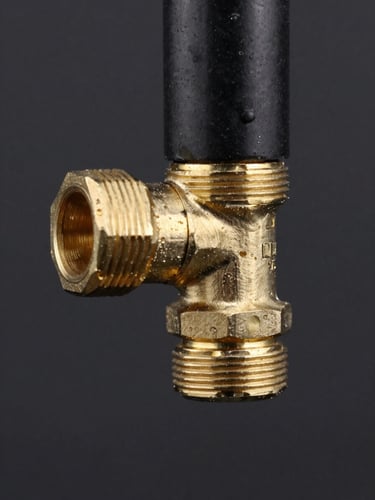 Macro technical photography of a brass elbow fitting connected to a black plastic pneumatic tube, high contrast studio lighting on a dark background