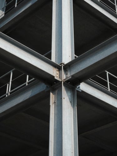 A high-contrast, low-angle architectural shot of sharp steel and concrete structural joints under cool, crisp daylight with deep shadows.