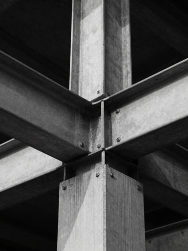 Symmetrical eye-level architectural detail of structural steel and concrete joints, sharp directional light, deep shadows, high-contrast black and white style.