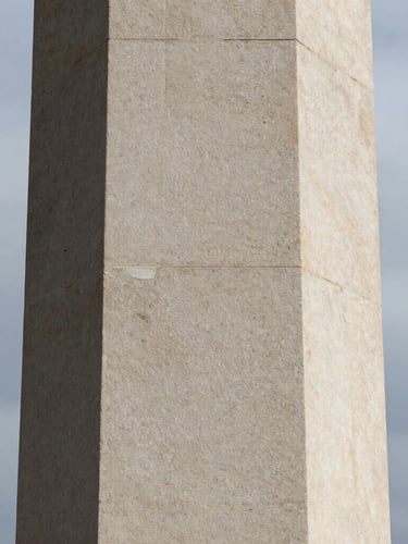 Extreme close-up of a monolithic limestone pillar, sharp shadows, overcast daylight, minimalist architectural texture.