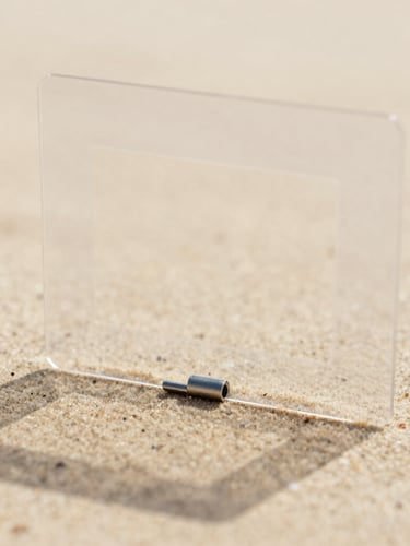 Close-up shot of a transparent acetate frame hinge, showing the delicate metal core, soft shadows, warm sand background, 35mm photography
