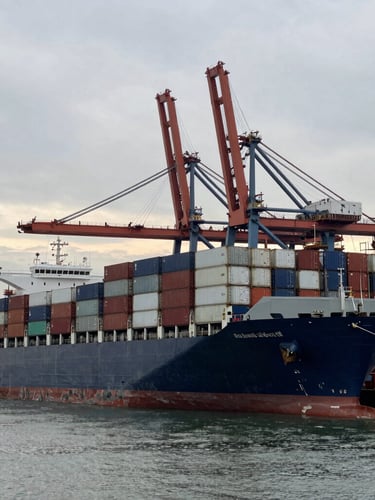 Wide environmental shot of a massive container vessel docking at a deepwater industrial port under early morning overcast sky, desaturated steel and navy tones, sharp focus, 35mm lens.