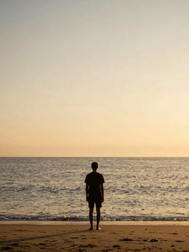 Solitary figure in silhouette, standing on a beach at golden hour, looking out at the vast ocean horizon, expansive sky, warm light.