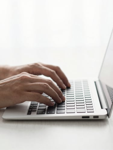 Close-up of hands typing on a sleek, minimalist keyboard, clean desk surface, soft natural light, cool gray tones, editorial composition