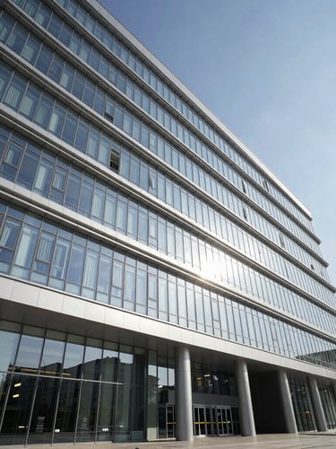 Wide angle architectural photo of a modern hospital facade in Baku, cool daylight, high-contrast shadows, silver-metallic reflections on glass.
