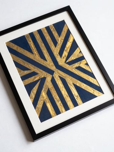Overhead flat-lay on white surface, single framed art print with bold geometric pattern in navy and gold, studio lighting, sharp edges, no props