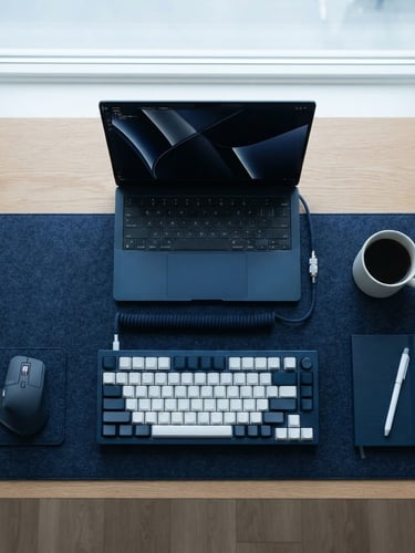 Symmetrical overhead shot of a clean minimalist desk setup in cool diffused Nordic daylight, a sleek laptop and metal mechanical keyboard, deep navy and white tones