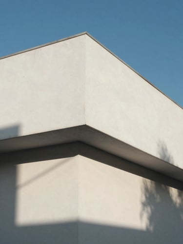 Composición geométrica minimalista de una fachada de hormigón blanco bajo luz solar directa, sombras duras y líneas puras, cielo azul despejado al fondo.