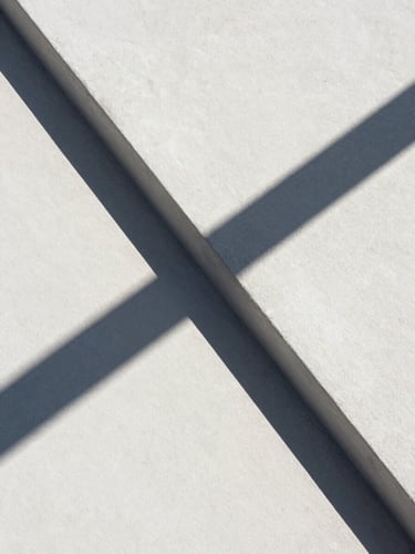 Extrema composición geométrica de una intersección de hormigón blanco bajo luz solar directa, sombras duras diagonales cruzando la superficie, estética de formato medio limpia y abstracta.