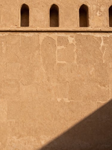 High-contrast architectural photograph of a restored Omani fortress wall, showing the seamless transition from ancient crumbling mudbrick to reinforced modern lime mortar