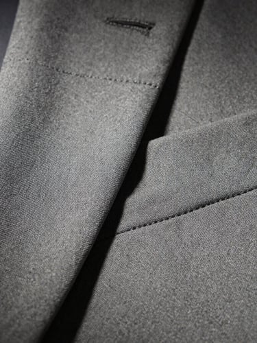 Macro detail shot of premium fabric texture and precise stitching on a tailored garment, dramatic industrial lighting, concrete tones, sharp focus, 35mm lens