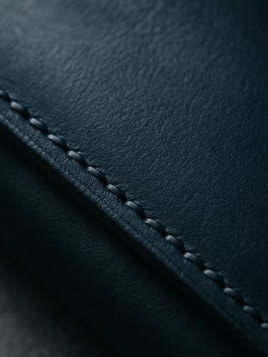 Extreme close-up of dark hand-stitched leather notebook cover, soft natural overcast daylight, rich texture, deep navy tones, editorial photography.