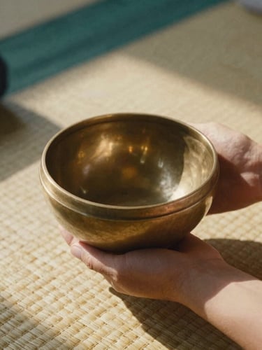 Close-up of hands holding a warm brass singing bowl on a woven grass mat, soft golden-hour sunlight casting deep natural shadows, earthy terracotta tones, 35mm film texture