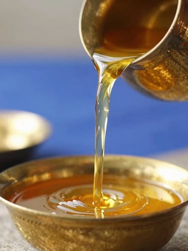 Close-up of traditional Indian brassware, golden ghee being poured slowly from a small brass vessel, warm morning light, shallow depth of field