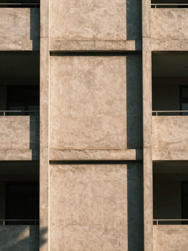 Straight-on architectural shot of a concrete building facade with sharp geometric shadows, minimalist composition, warm sand tone, 35mm