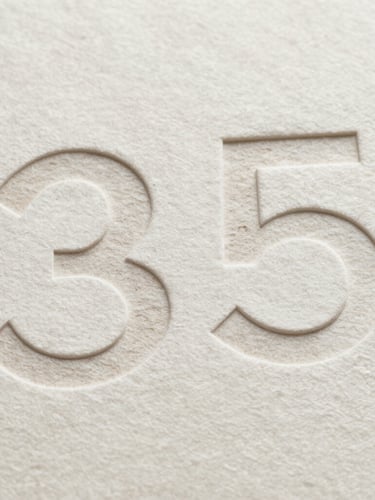Extreme close-up of heavy cotton paper stock with deeply debossed minimalist typography, sharp geometric shadows, neutral studio light, 35mm