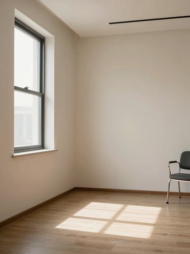 Empty therapy room interior, natural diffused light from a tall window on the left, clean architectural lines, warm off-white walls, a single chair in the far right corner, sparse and precise