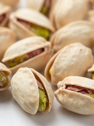 Macro close-up of graded raw pistachio kernels on a clean neutral surface, bright clinical studio lighting, sharp focus on texture.