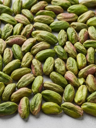 Macro close-up of graded raw pistachio kernels on a clean, light gray neutral surface, bright clinical studio lighting, sharp focus.