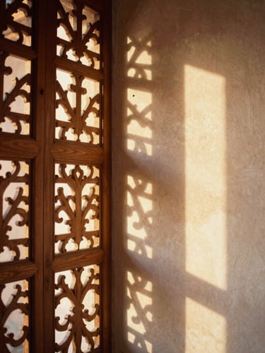 Soft golden-hour light filtering through a carved cedarwood screen, casting warm geometric shadows on a tadelakt plaster wall, 35mm editorial photography.