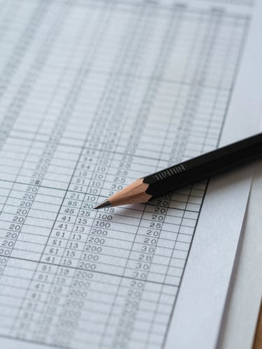 Overhead close-up of a financial spreadsheet and a mechanical pencil resting on ruled paper, cool north-facing daylight, precise analytical work in progress, no people