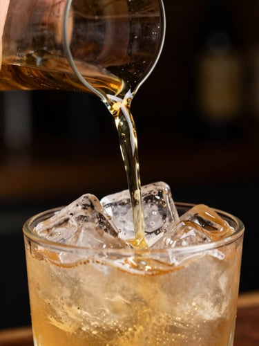 Extreme close-up of a hand pouring a perfectly measured golden cocktail over clear ice, dark moody background, warm brass lighting.