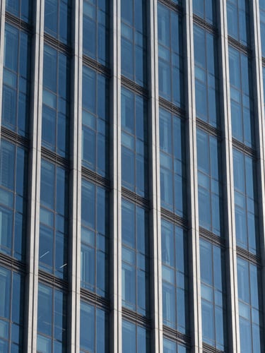 Crisp architectural photography of a modern glass and steel financial skyscraper facade, sharp high-contrast daylight with deep shadows, cobalt blue tones, 35mm